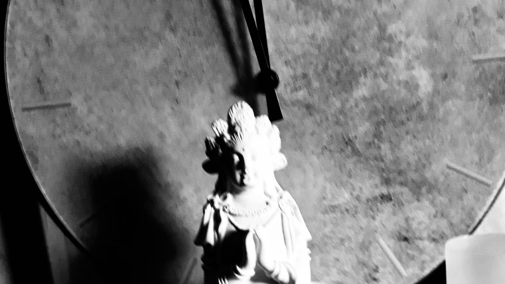 Statue mit gefalteten Händen vor einer Uhr mit Zeigern.